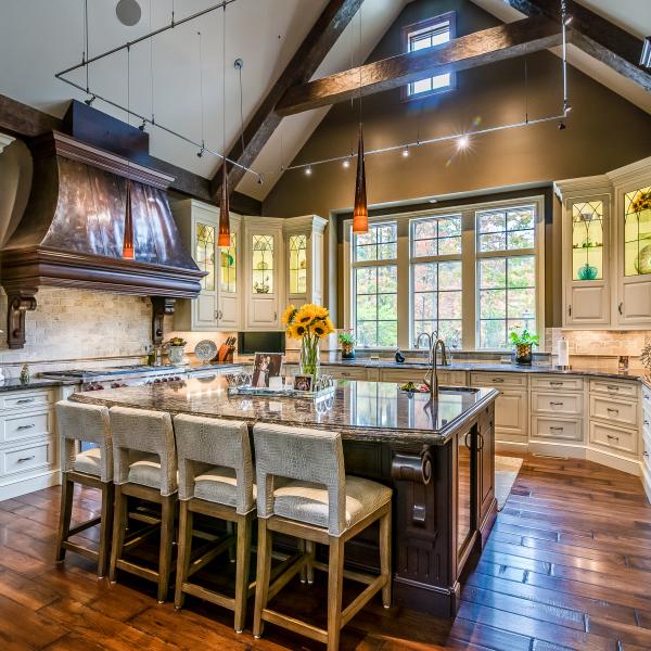 A custom-built, cathedral-style kitchen with exposed wood beams, hardwood floors, and a large island with seating for four.