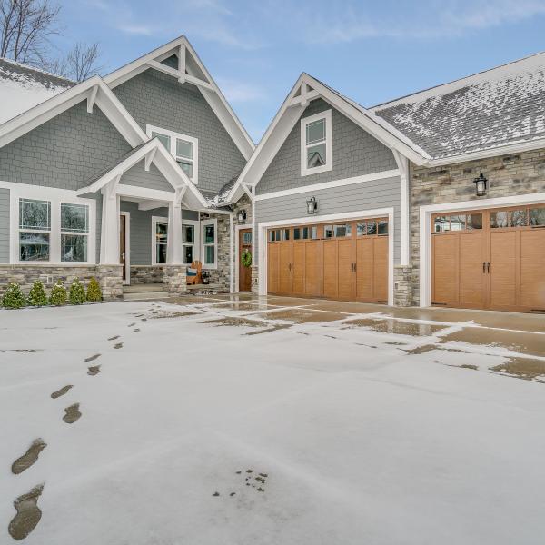 Large 3-car, stone garage connected to custom-built home and cement driveway near lake.