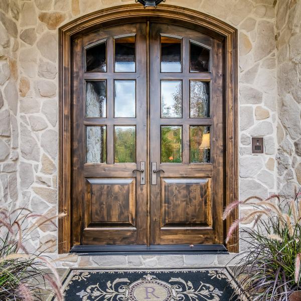 Large cathedral exterior doors surrounded by stone walls, a stone walkway and hardwood ceiling. 