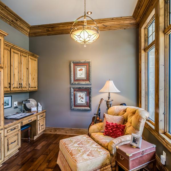 An office featuring built-in wood cabinets and a desk is well lit thanks to the ample lighting and large windows.